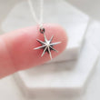 Load image into Gallery viewer, North Star, Starburst pendant in sterling silver on cable chain, on finger with white background. By Studio Blue on Etsy