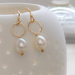 Load image into Gallery viewer, White, oval freshwater pearl drop earrings featuring a delicate open hoop in 14k Gold fill shown on white vessel with tiny holes, by Studio Blue on Etsy