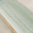 Load image into Gallery viewer, Dainty paperclip link chain necklace shown in 14k gold fill, and Sterling silver shown on a light green oblong ceramic dish. By Studio Blue on Etsy