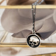 Load image into Gallery viewer, Sterling silver Skull medallion with an oxidized, dotted silver chain, in a brass and glass box with brown ribbon. By Studio Blue on Etsy