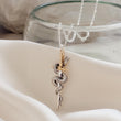 Load image into Gallery viewer, Close-up of the Snake &amp; Dagger Necklace on cream fabric
