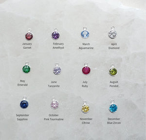 Studio Blue’s 12 gemstone options for customizing the Snake & Dagger Necklace: Garnet (January), Amethyst (February), Aquamarine (March), Clear Quartz (April), Emerald (May), Moonstone (June), Ruby (July), Peridot (August), Sapphire (September), Pink Tourmaline (October), Citrine (November), and Blue Topaz (December). Each gemstone adds a personal touch to this handcrafted pendant.