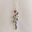 Load image into Gallery viewer, Detailed view of the Snake &amp; Dagger Necklace pendant showing the curved serpent wrapping around the dagger’s blade, crafted in sterling silver with bronze-gold accents for an edgy, statement finish and a red gemstone
