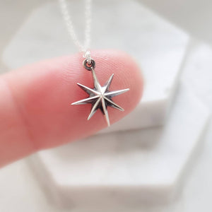 North Star, Starburst pendant in sterling silver on cable chain, on finger with white background. By Studio Blue on Etsy