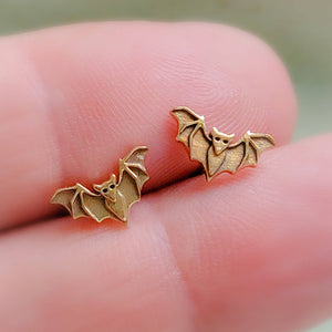 Golden bronze little bat studs between 2 fingers, by Studio Blue on Etsy