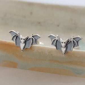 Sterling silver little bat studs on the rim of a sage green dish, by Studio Blue on Etsy