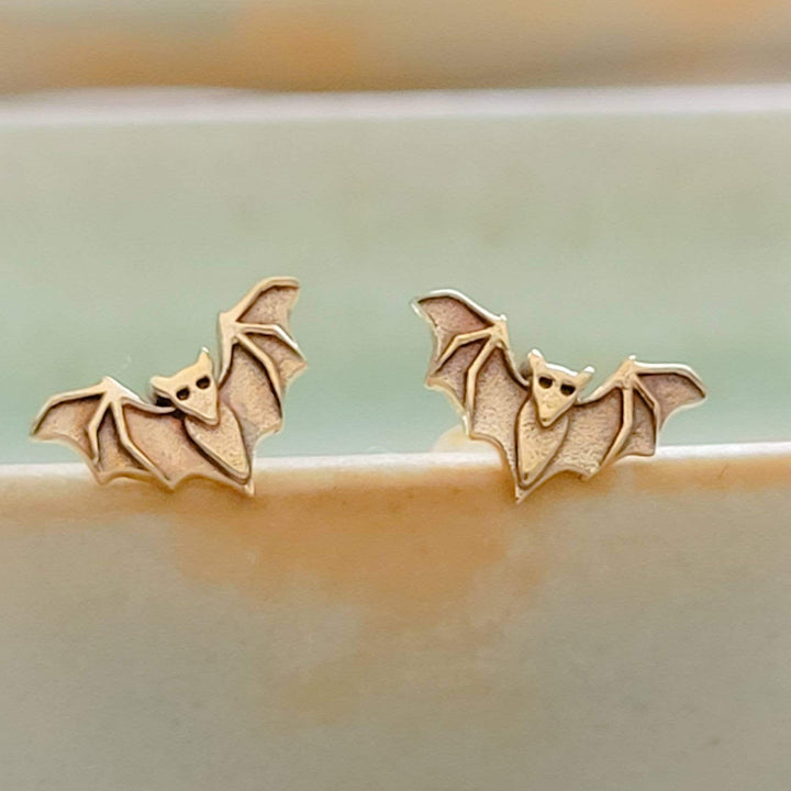 Golden bronze little bat studs on the rim of a sage green dish, by Studio Blue on Etsy