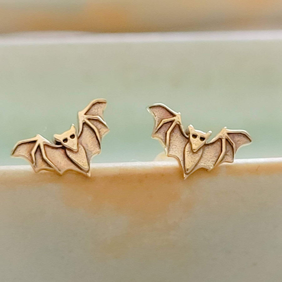 Golden bronze little bat studs on the rim of a sage green dish, by Studio Blue on Etsy