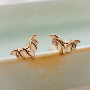 Golden bronze little bat studs on the rim of a sage green dish, by Studio Blue on Etsy