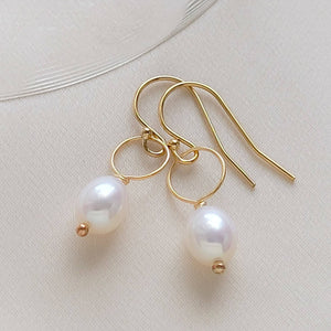 White, oval freshwater pearl drop earrings featuring a delicate open hoop in 14k Gold fill shown on beige background, by Studio Blue on Etsy