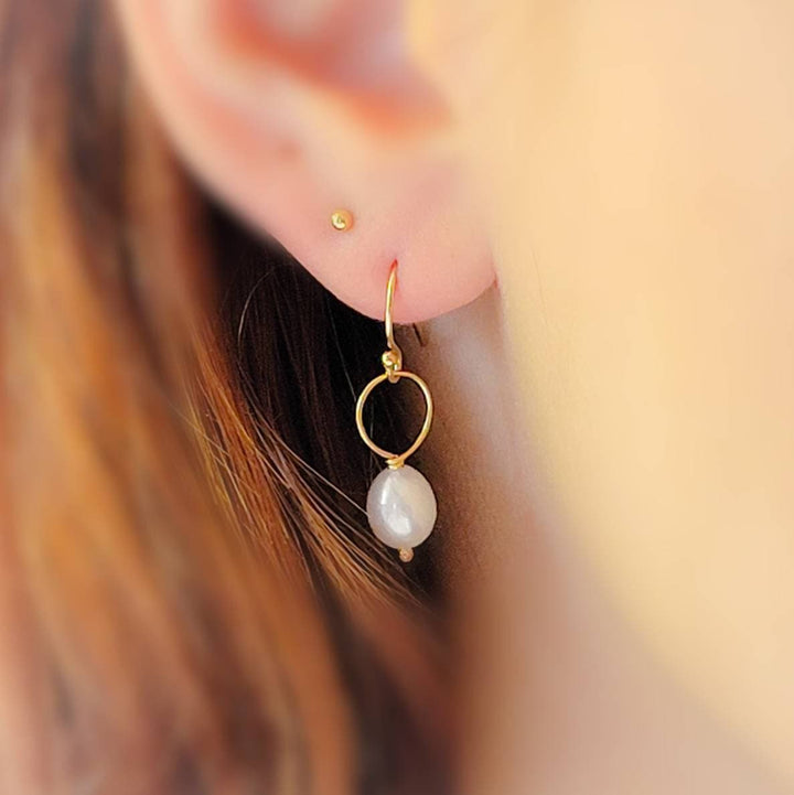 White, oval freshwater pearl drop earrings featuring a delicate open hoop in 14k Gold fill shown on model, by Studio Blue on Etsy