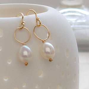 White, oval freshwater pearl drop earrings featuring a delicate open hoop in 14k Gold fill shown on white vessel with tiny holes, by Studio Blue on Etsy