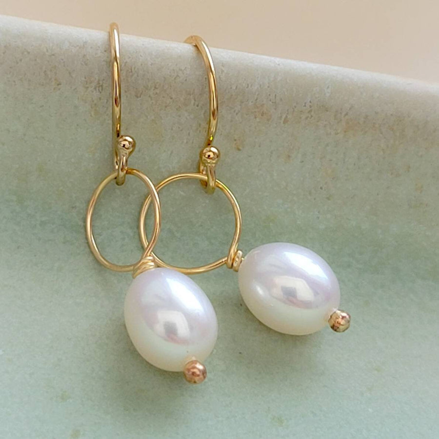 White, oval freshwater pearl drop earrings featuring a delicate open hoop in 14k Gold fill shown on pale green background, by Studio Blue on Etsy