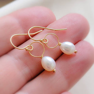 White, oval freshwater pearl drop earrings featuring a delicate open hoop in 14k Gold fill shown in hand, by Studio Blue on Etsy