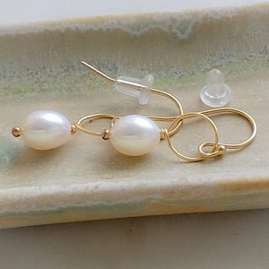 White, oval freshwater pearl drop earrings featuring a delicate open hoop in 14k Gold fill with rubber ear backs shown on a pale green ceramic dish, by Studio Blue on Etsy