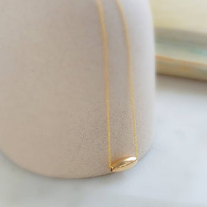 Gold fill oval bead floating on a dainty chain, on a tan vessel, by Studio Blue on Etsy