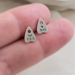 Sterling Silver Ouija Board-inspired stud earrings between two fingers. Yes & No, Moon & Star. By Studio Blue on Etsy