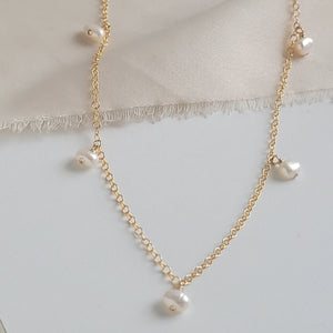 White Baroque pearl drops on delicate 14k gold fill chain, shown on a beige and white background, by Studio Blue on Etsy