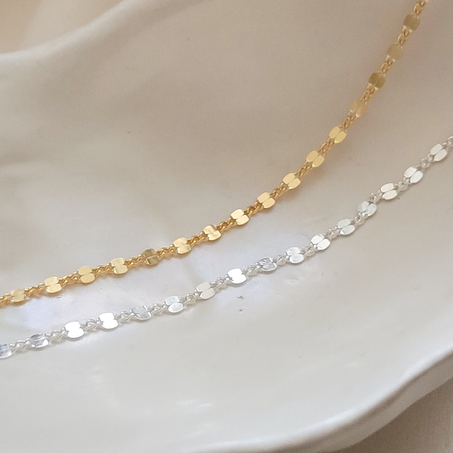 Dainty shimmer chain shown in 14k gold fill & sterling silver on cream colored dish by Studio Blue on Etsy