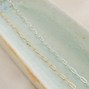 Dainty paperclip link chain necklace shown in 14k gold fill, and Sterling silver shown on a light green oblong ceramic dish. By Studio Blue on Etsy