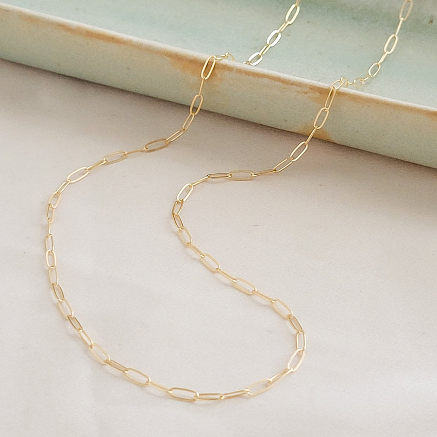 Dainty paperclip link chain necklace shown in 14k gold fill, shown draped on a light green oblong ceramic dish and beige background. By Studio Blue on Etsy