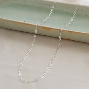 Dainty paperclip link chain necklace shown in Sterling silver, shown draped on a light green oblong ceramic dish and beige background. By Studio Blue on Etsy