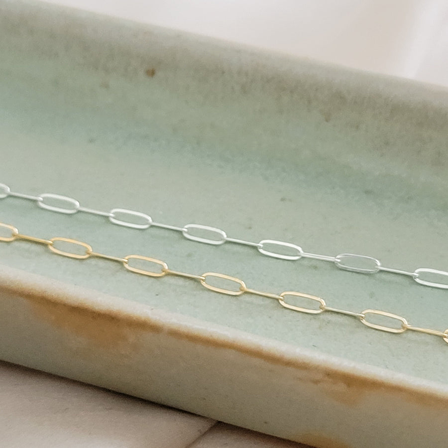 Dainty paperclip link chain necklace shown in 14k gold fill, and Sterling silver shown on a light green oblong ceramic dish. By Studio Blue on Etsy