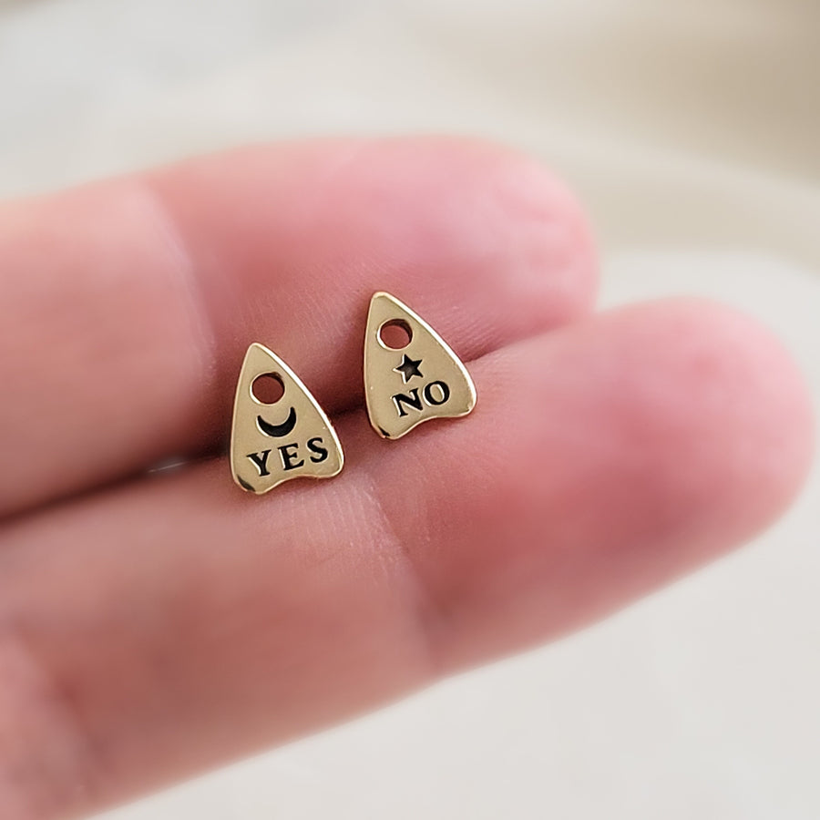 Bronze Ouija Board-inspired stud earrings between two fingers. Yes & No, Moon & Star. By Studio Blue on Etsy