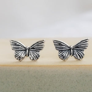 Pair of Sterling silver Butterfly studs earrings shown on a sage green and tan ceramic dish, by Studio Blue on Etsy