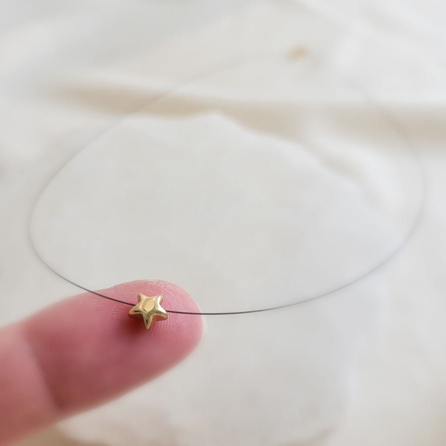 Golden Pyrite Star necklace on black filament, shown on index finger by Studio Blue on Etsy