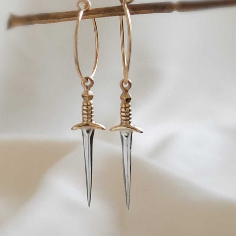 Bronze & Sterling Silver Dagger charm on a 15mm Gold fill hoop earring, shown dangling from a twig. By Studio Blue on Etsy