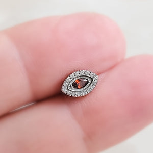 Titanium Evil Eye earring stud with pavé set clear CZ&#39;s around a red, marquise shaped CZ in the center, held between 2 fingers By Studio Blue on Etsy