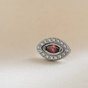 Titanium Evil Eye earring stud with pavé set clear CZ&#39;s around a red, marquise shaped CZ in the center, on a cream-colored background, by Studio Blue on Etsy