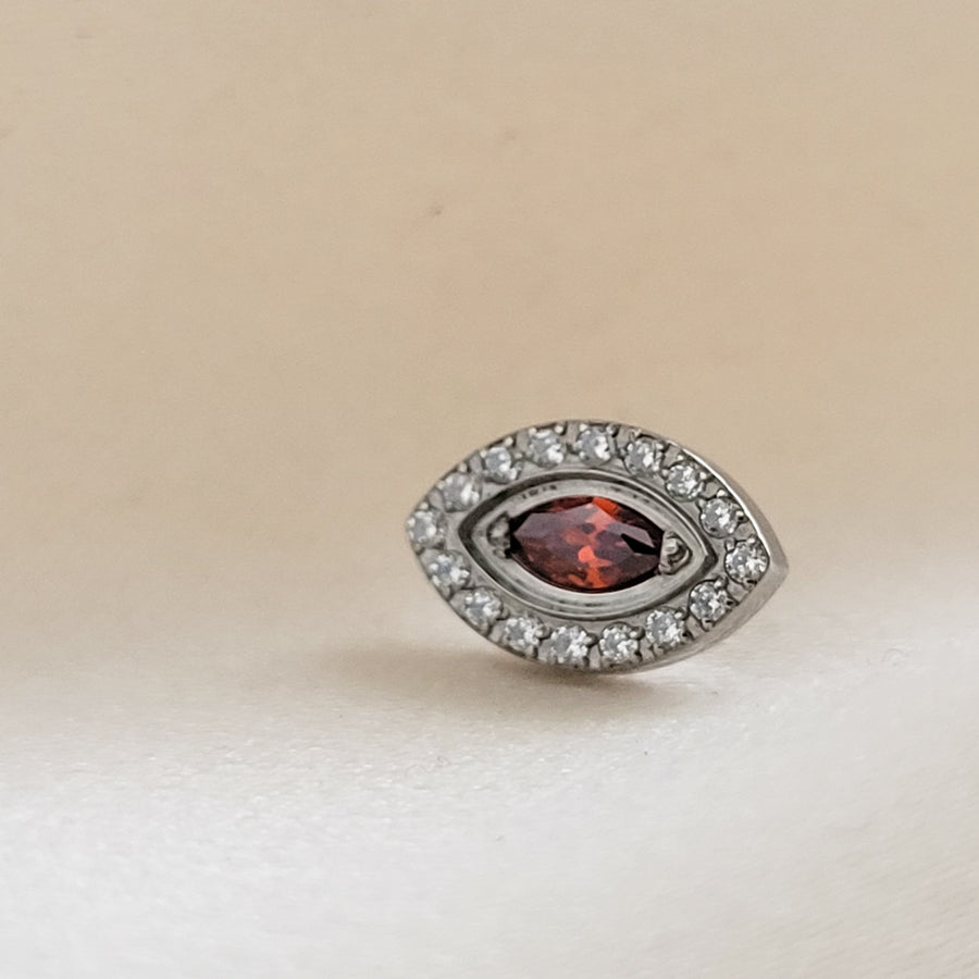 Titanium Evil Eye earring stud with pavé set clear CZ&#39;s around a red, marquise shaped CZ in the center, on a cream-colored background, by Studio Blue on Etsy